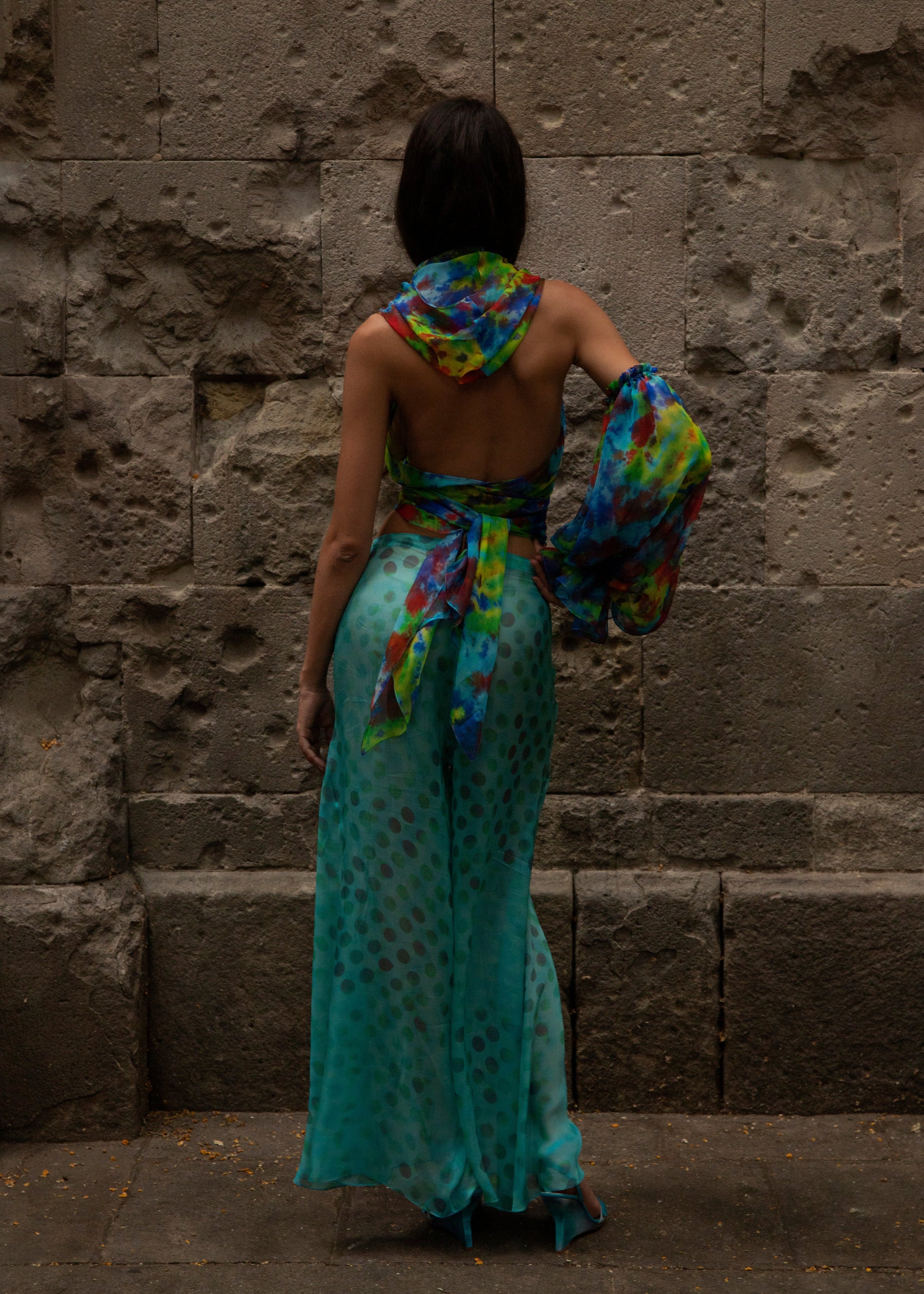 Woman in Dramatica pants in acqua salata and Angelica top in Daydream against a stone wall.