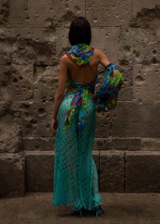 Woman in Dramatica pants in acqua salata and Angelica top in Daydream against a stone wall.