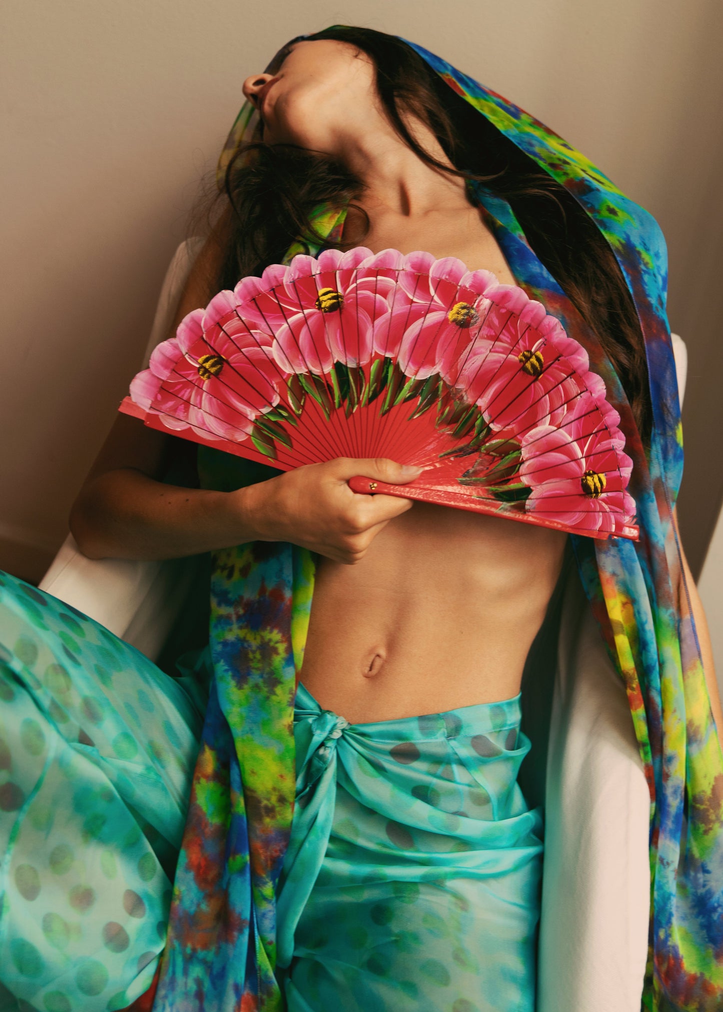 Woman in Dramatica pants in acqua salata and Angelica top in Daydream with colorful patterns holding a pink fan
