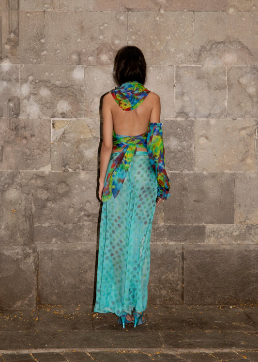 Woman in Dramatica pants in acqua salata with colorful patterns against a stone wall.