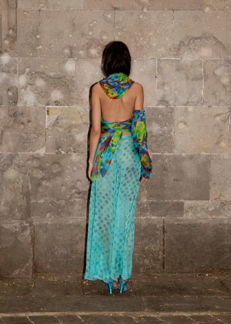 Woman in Dramatica pants in acqua salata with colorful patterns against a stone wall.