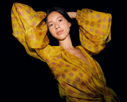 Woman wearing Electrica blouse in Honeybaby against a black background