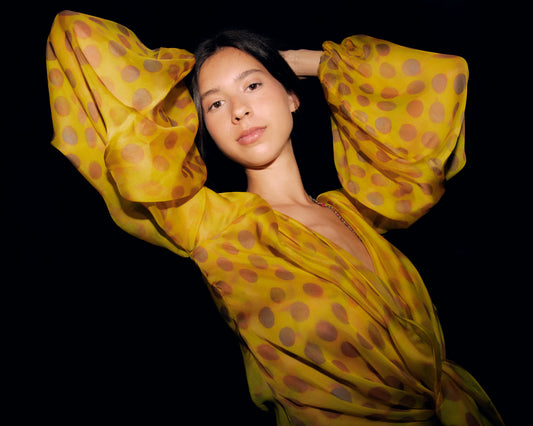 Woman wearing Electrica blouse in Honeybaby against a black background