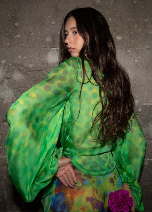 Woman wearing Electrica blouse in 4leaf clover against a stone wall.
