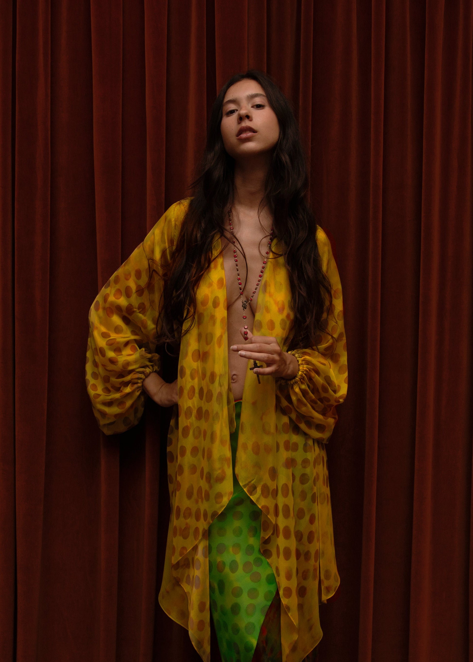 Woman wearing Electrica blouse in Honeybaby against a red curtain background