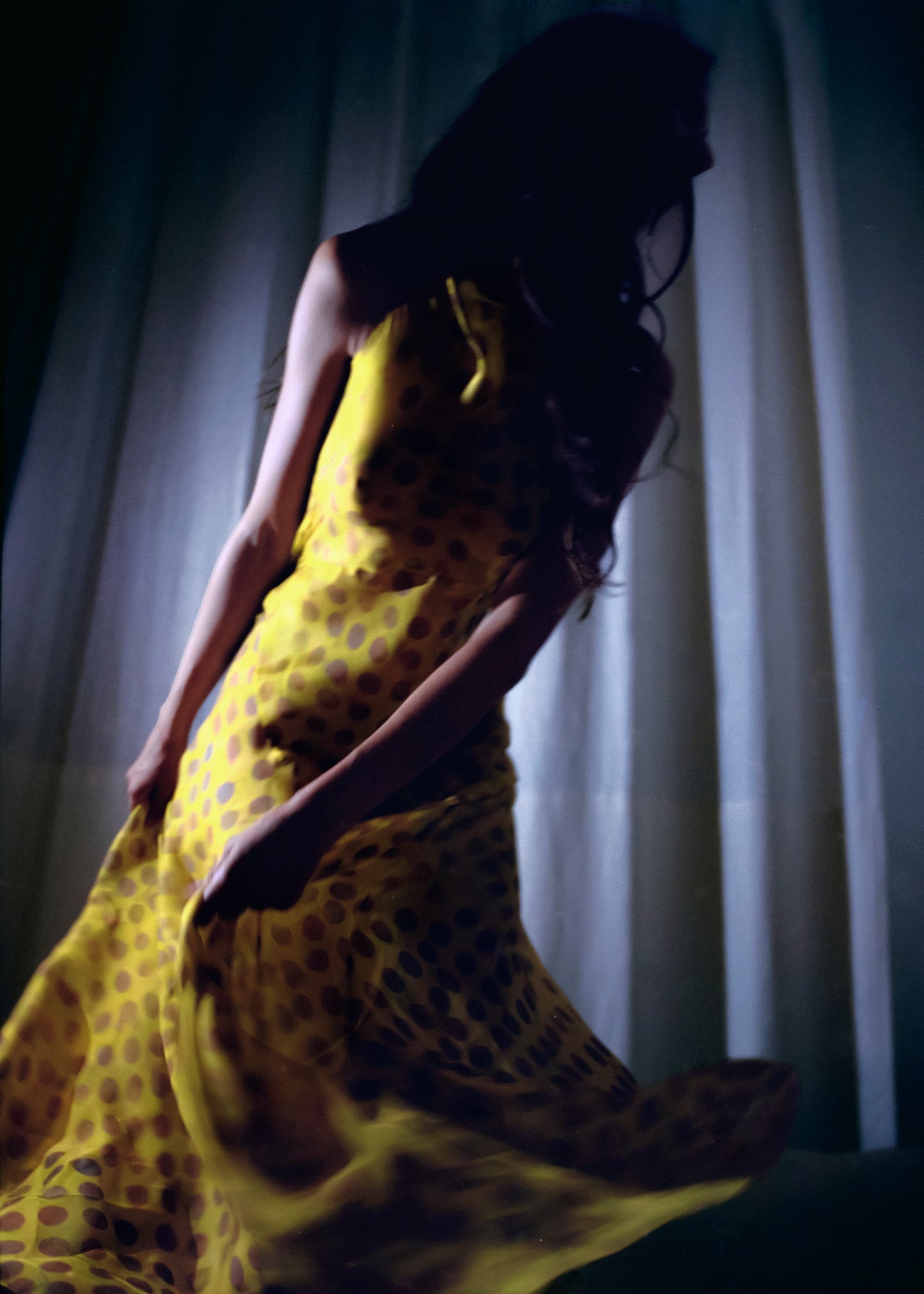 Woman in Romantica dress in Honeybaby  sitting against a white curtain.