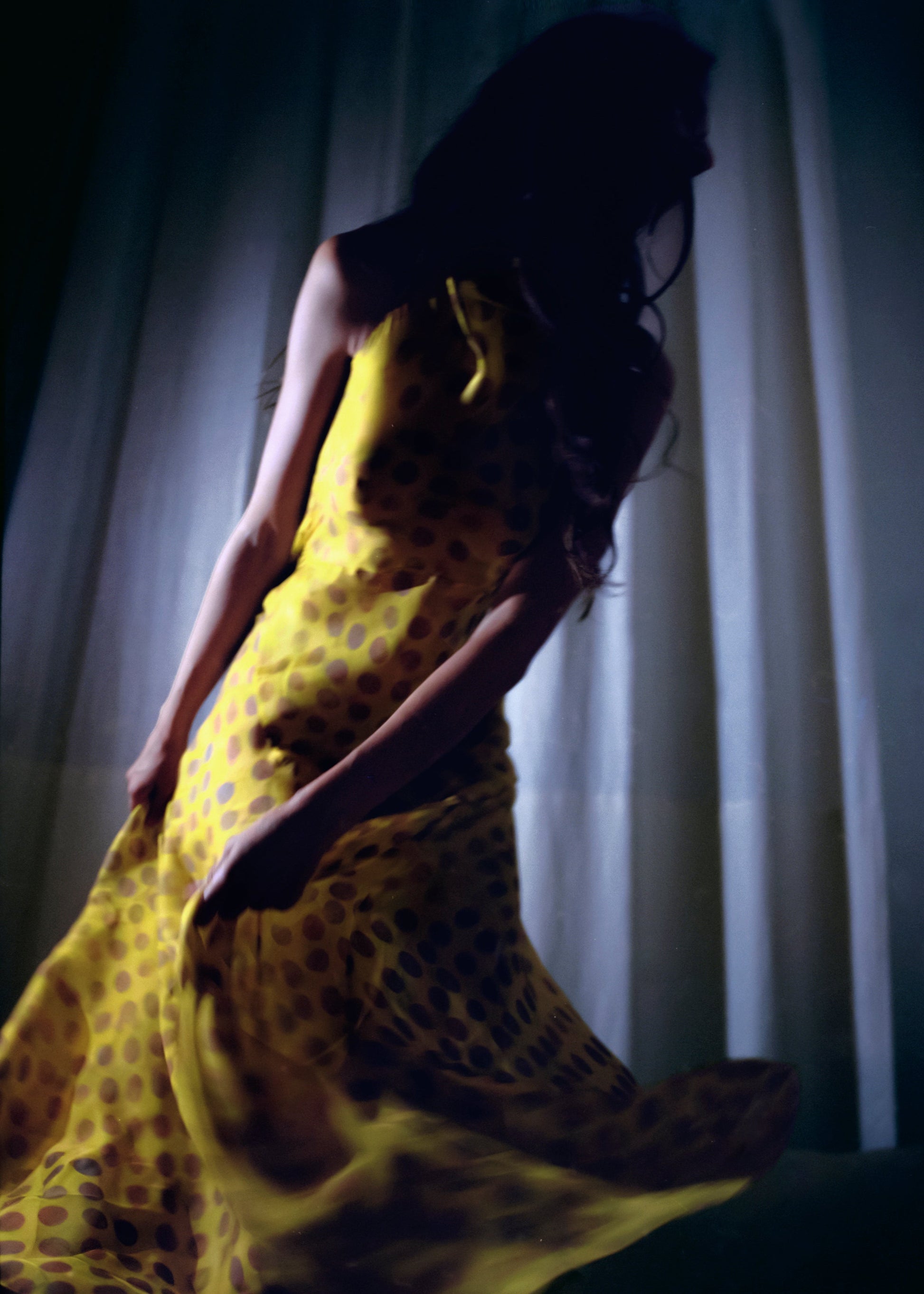 Woman in Romantica dress in Honeybaby  sitting against a white curtain.
